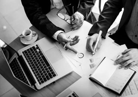 Two people in business suits reviewing and signing documents at a table